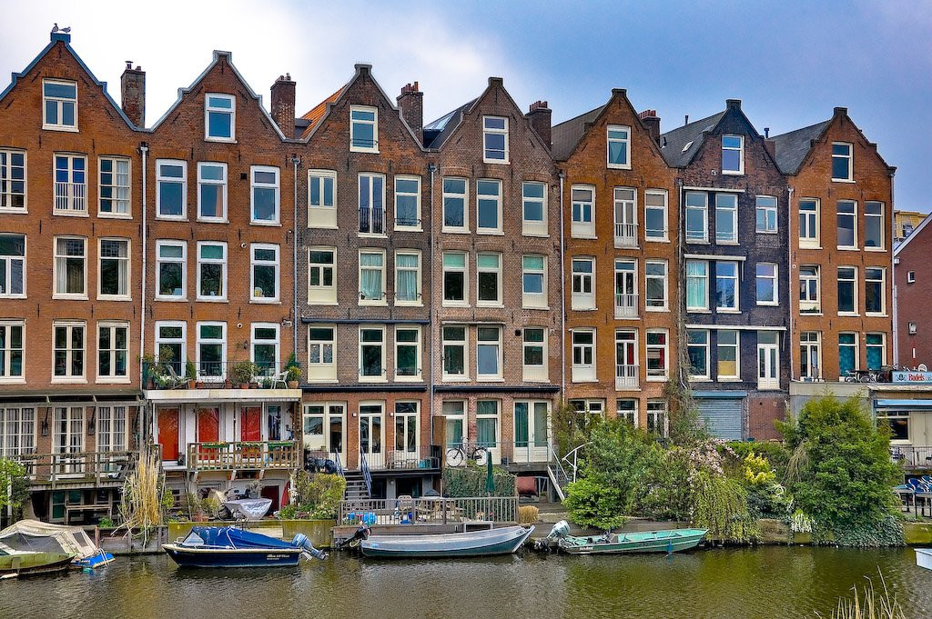Жилой дом с припаркованными катерами в Амстердаме, Нидерланды – фотографии Нидерландов