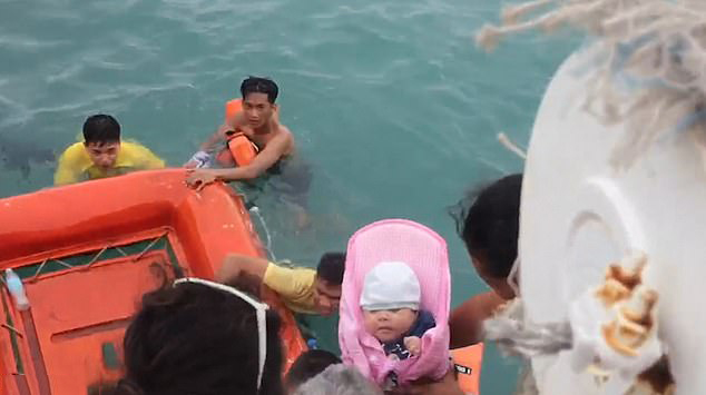 На воду опущена надувная шлюпка, куда один из пассажиров передаёт завернутого в одеяло новорождённого ребёнка